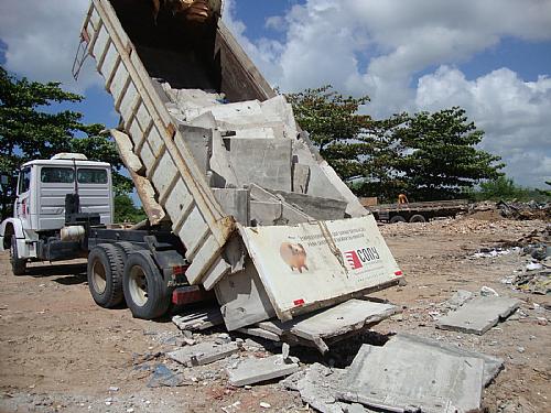 Caçamba da Cony Engenharia descarregando placas de concreto num terreno no Dique Estrada