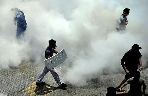 Manifestantes caminham em meio a gás lacrimogênio jogado pela polícia.