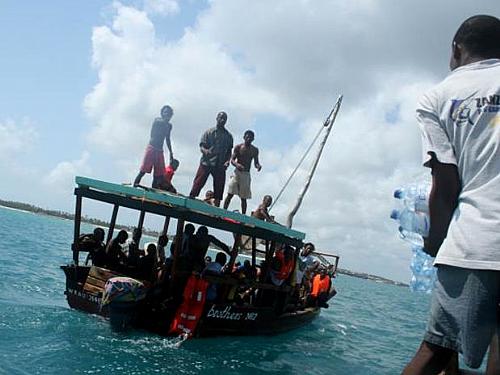 Homens em um barco de turismo jogam garrafas de água para sobreviventes resgatados