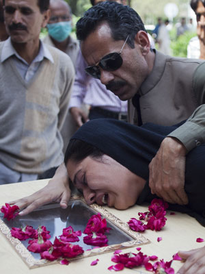 Homem conforta mulher que chora sobre o caixão de familiar morto no acidente aéreo, em hospital de Islamabad
