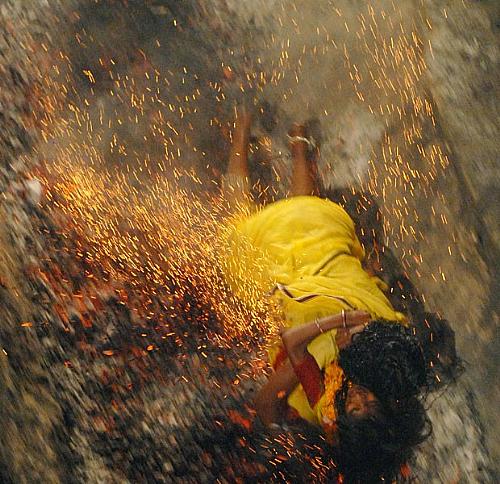Devota hindu cai em carvão quente enquanto segura a filha durante uma corrida sobre carvão na Índia